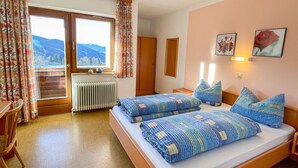 Un dormitorio con dos camas, piso de madera, ventana con vistas a montañas, un radiador y una silla.