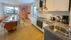 Una cucina moderna con zona pranzo, caratterizzata da un tavolo lungo apparecchiato per sei persone, un forno a incasso e una macchina da caffè.