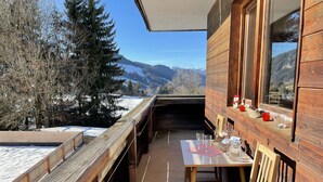 Un terrazzo in legno con tavolo e sedie, affacciato su un paesaggio innevato e montagne.