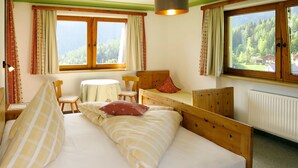 A cozy room with a wooden bed, a small table, and a chair. There are two windows with curtains, and a radiator is visible on the wall. - Mitterer by Interhome (Finkenberg)