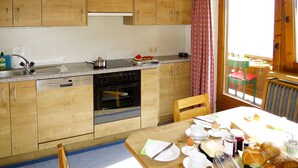 A compact kitchen with wooden cabinets, a Siemens dishwasher, a stove, and a dining area with a table set for breakfast. - Mitterer by Interhome (Finkenberg)