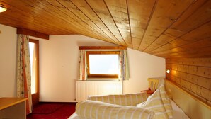 A cozy room with a wooden ceiling, a bed with striped bedding, a window with curtains, and a radiator. - Mitterer by Interhome (Finkenberg)