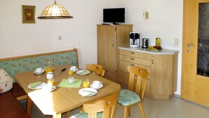 A cozy dining area with a wooden table and chairs, a television above the cabinets, and a fruit bowl on the counter. - Mitterer by Interhome (Finkenberg)