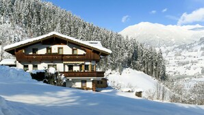 A two-story chalet with a snow-covered roof, surrounded by a snowy landscape and forested mountains. - Apartment Markus by Interhome (Zell am Ziller)