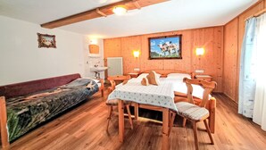 A cozy room with wooden walls, a wooden dining table with chairs, a sofa, and a bed.