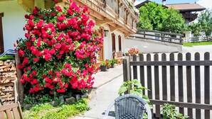A wooden outdoor seating area with a table and chairs, a wooden fence, and a building with a balcony adorned with flowers.