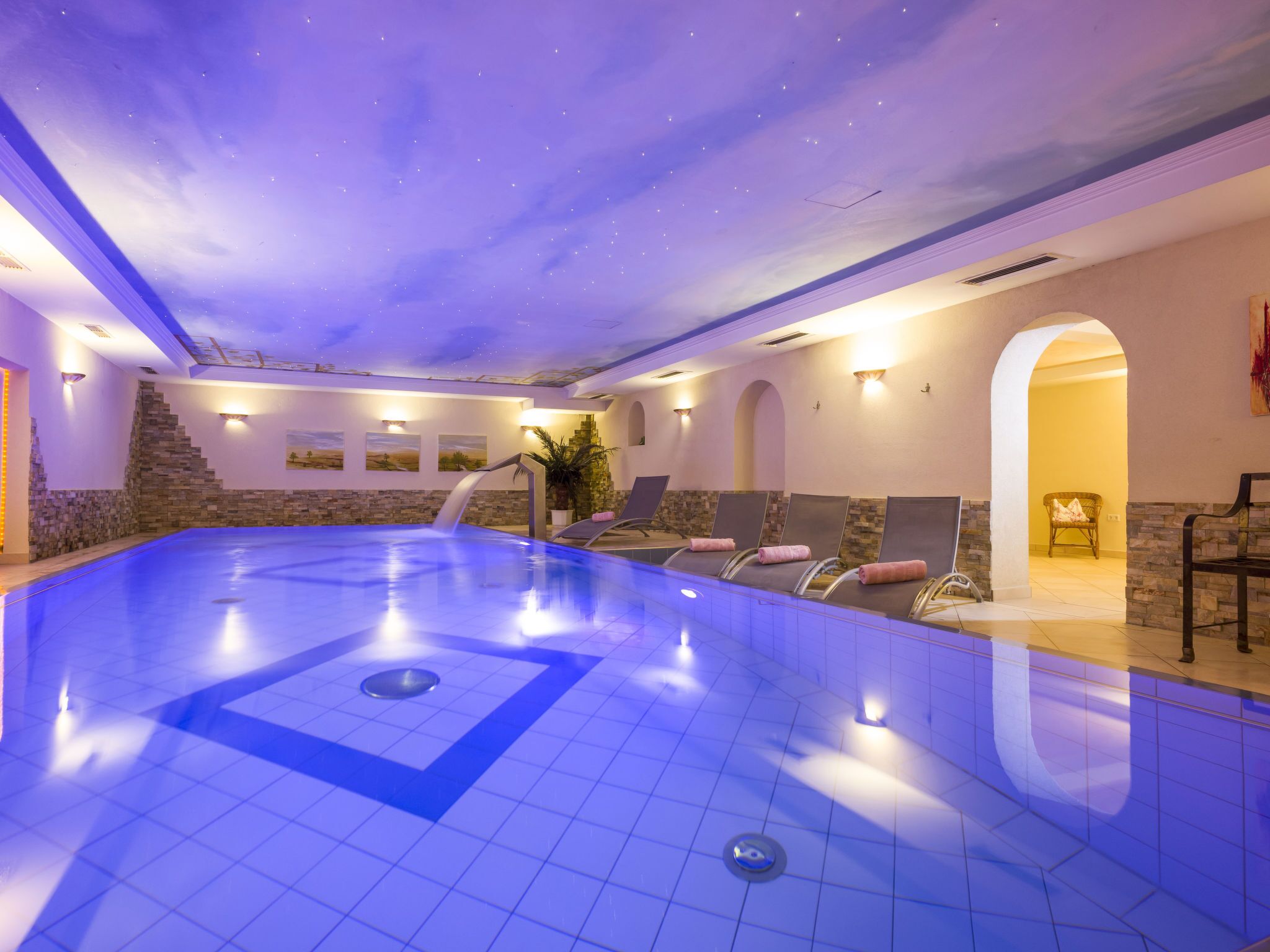 A large indoor swimming pool with a starry ceiling, stone walls, and multiple lounge chairs.