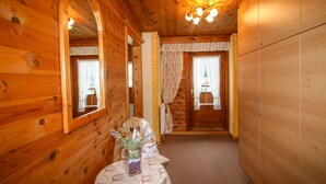 A wooden cabin interior with a wooden door, a mirror, a table with a vase, and a chandelier.