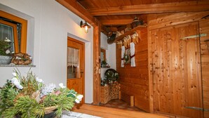 A wooden interior with a wooden door, a window with curtains, a wooden ceiling, and a table with a floral arrangement.