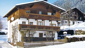 A two-story wooden chalet with a balcony, surrounded by snow-covered mountains.