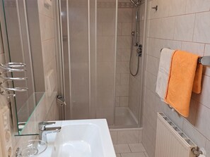 A bathroom with a glass shower enclosure, a white sink, and a towel rack with an orange towel. - Waldfrieden by Interhome (Mondsee)