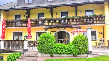 Ein gelbes Gebäude mit Balkon, Außenbestuhlung und einer Treppe zum Eingang.