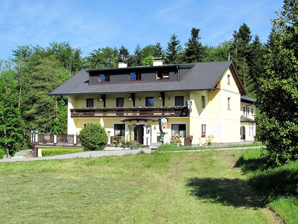 A two-story building with a balcony, a sign indicating a restaurant, and a view of the surrounding forest. - Waldfrieden by Interhome (Mondsee)