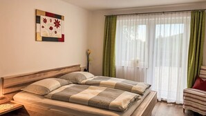 A neatly made bed with striped bedding, a bedside table with a lamp, a green chair, and a window with sheer curtains. - Mayrhofer by Interhome (Mondsee)