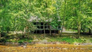 A cabin surrounded by dense forest with a clear stream in the foreground. - Riverside relaxation and all the comforts of home! - Aska River House (Blue Ridge)