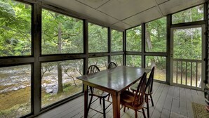 A covered outdoor dining area with a table and chairs, large windows, and a view of a river and forest. - Riverside relaxation and all the comforts of home! - Aska River House (Blue Ridge)