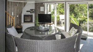 Un espacio al aire libre moderno con una mesa de vidrio y sillas de mimbre, un televisor de pantalla plana y una chimenea.