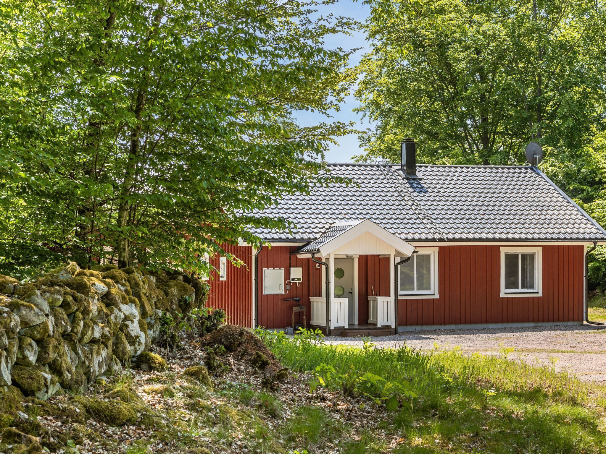 A red wooden house with a tiled roof, a porch, and a stone wall.