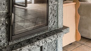 A stone fireplace with a glass door, a wooden bench, and a patterned cushion in a living room. - Erikstorp 143 by Interhome (Olofström)