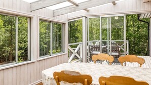 A sunroom with large windows, a wooden deck, and a table with chairs. - Erikstorp 143 by Interhome (Olofström)
