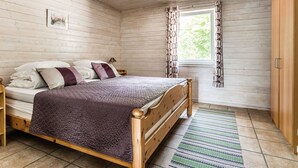 A wooden-paneled bedroom with a bed, a nightstand, a window with curtains, and a wooden wardrobe. - Erikstorp 143 by Interhome (Olofström)