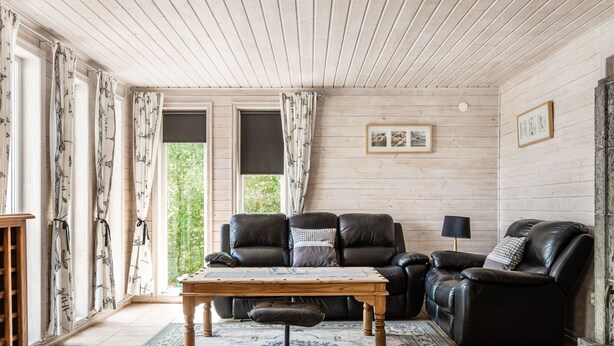 A cozy living room with a wooden ceiling, a leather sofa, a wooden coffee table, and a patterned rug. - Erikstorp 143 by Interhome (Olofström)