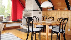 Un coin repas chaleureux avec une table et des chaises en bois, une cheminée en briques blanches et un rideau rouge.