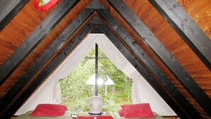 Une chambre mansardée chaleureuse, avec deux lits, une table de chevet rouge et une fenêtre donnant sur un paysage verdoyant.