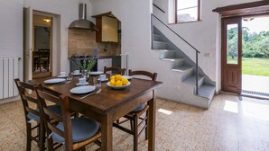 Un coin repas avec une table en bois dressée pour quatre personnes, une cuisine en arrière-plan et un escalier menant à un espace extérieur.