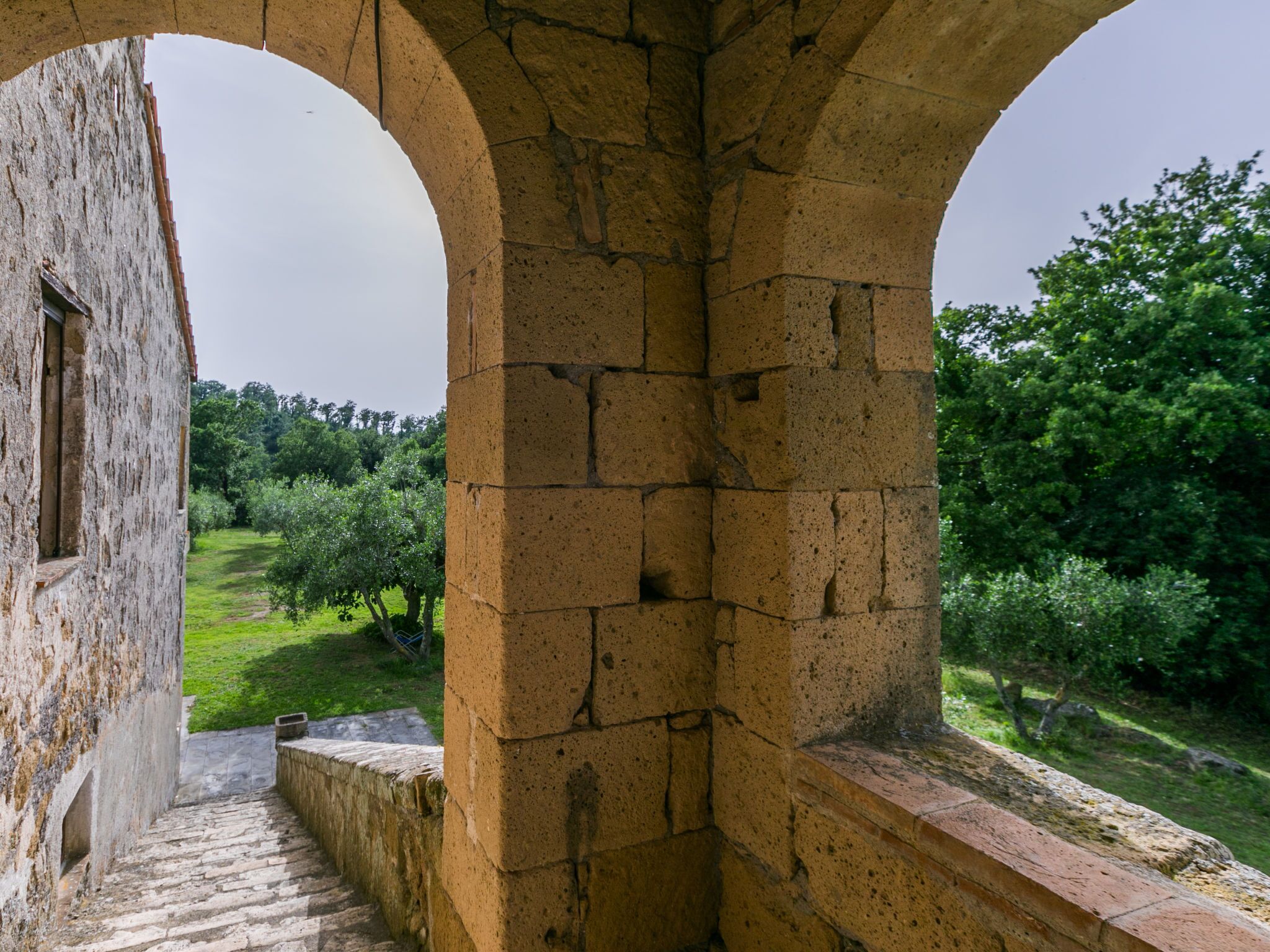 A stone archway leading to a courtyard with a view of a lush garden and trees.
