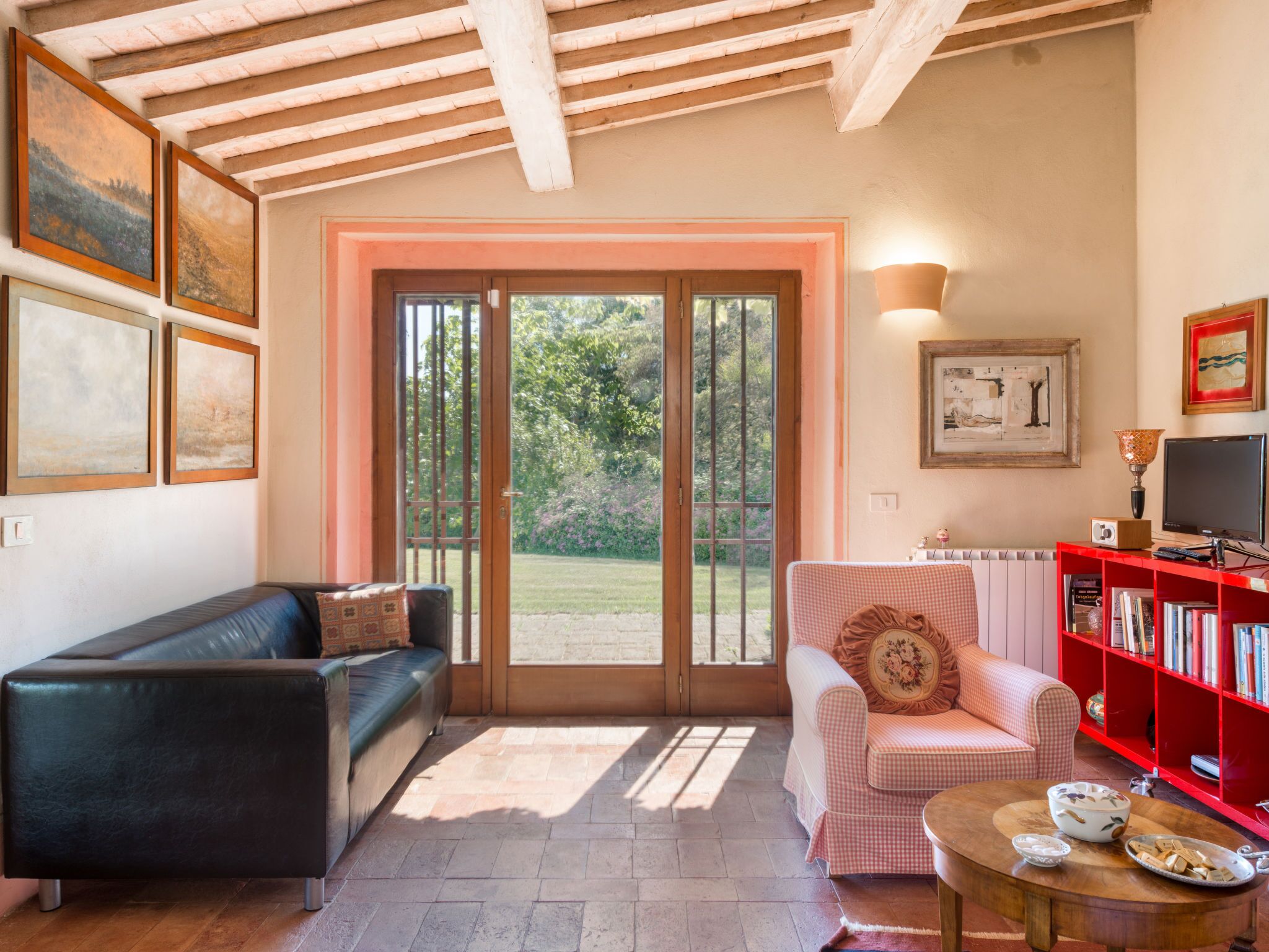 Una sala de estar con un sofá negro, un sofá rosa a cuadros, una estantería roja y una mesa de centro de madera.
