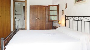 Une chambre avec une armoire en bois, un lit avec une tête de lit en métal, une table de chevet avec une lampe et un tableau accroché au mur.