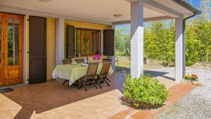 Un espace extérieur abrité, aménagé pour les repas, avec une table pour quatre personnes, entourée de chaises, et un petit jardin avec des plantes et des fleurs.