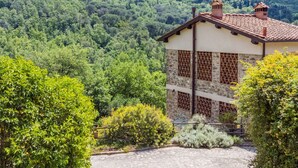 A stone building with a tiled roof, surrounded by lush greenery and a mountainous backdrop. - Policleto by Interhome (San Polo in Chianti)