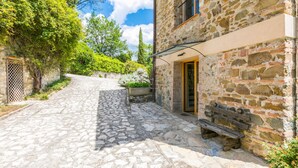 A stone building with a wooden door and a window, a stone pathway, and greenery. - Policleto by Interhome (San Polo in Chianti)