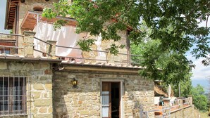 A stone building with a wooden balcony, a metal railing, and a door leading to an interior space. - Rondini by Interhome (San Polo in Chianti)
