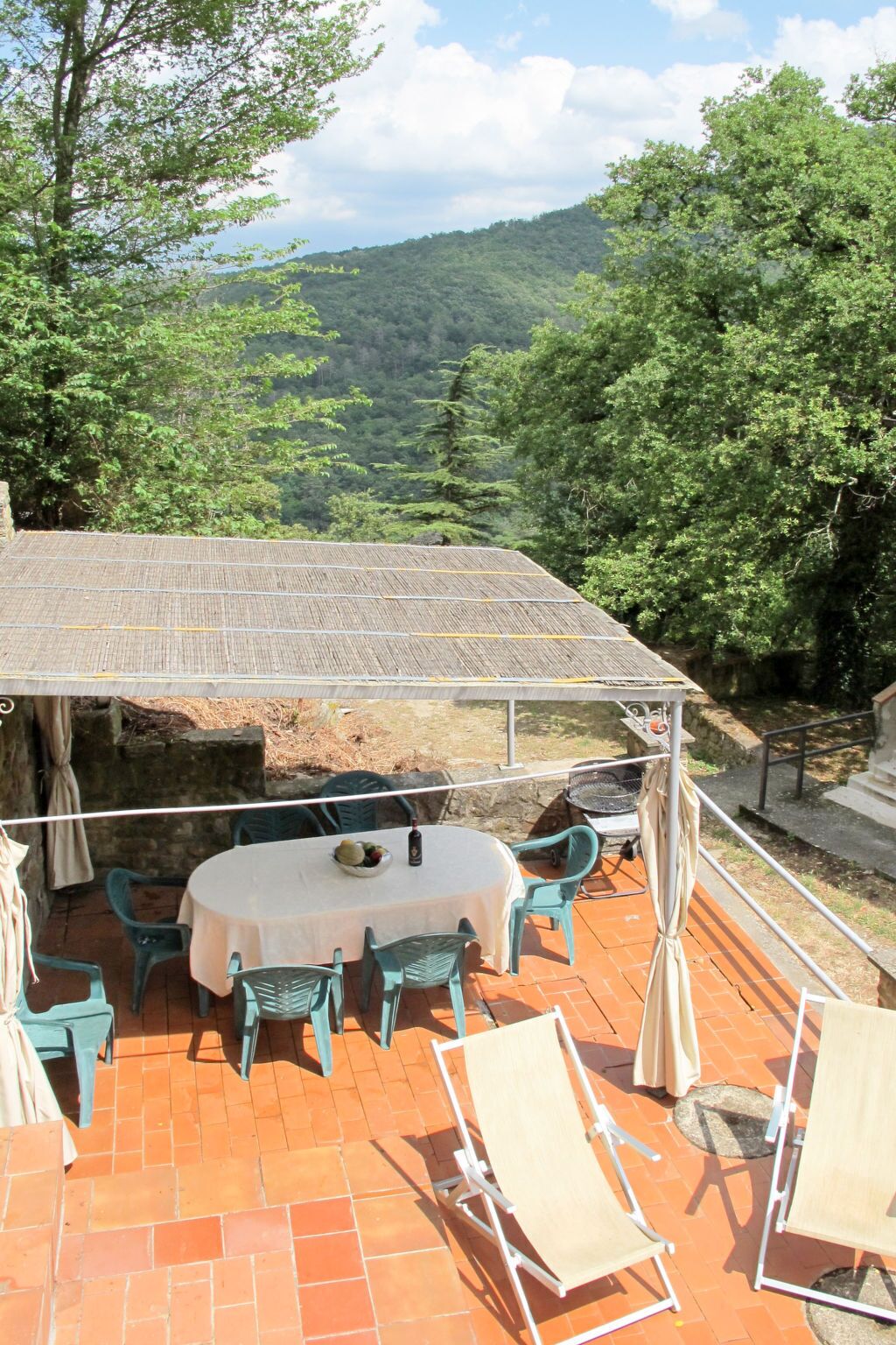 An outdoor patio with a table and chairs, a covered seating area, and a view of a forested valley.
