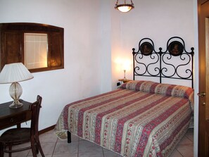 A bedroom with a bed, a desk with a lamp, a chair, a wall-mounted picture, and a hanging light fixture. - Vacation home Chiesa by Interhome (San Polo in Chianti)