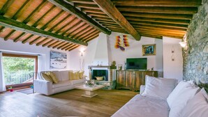Ein geräumiges Wohnzimmer mit hoher Holzbalkendecke, Kamin, Fernseher und einer Steinwand.