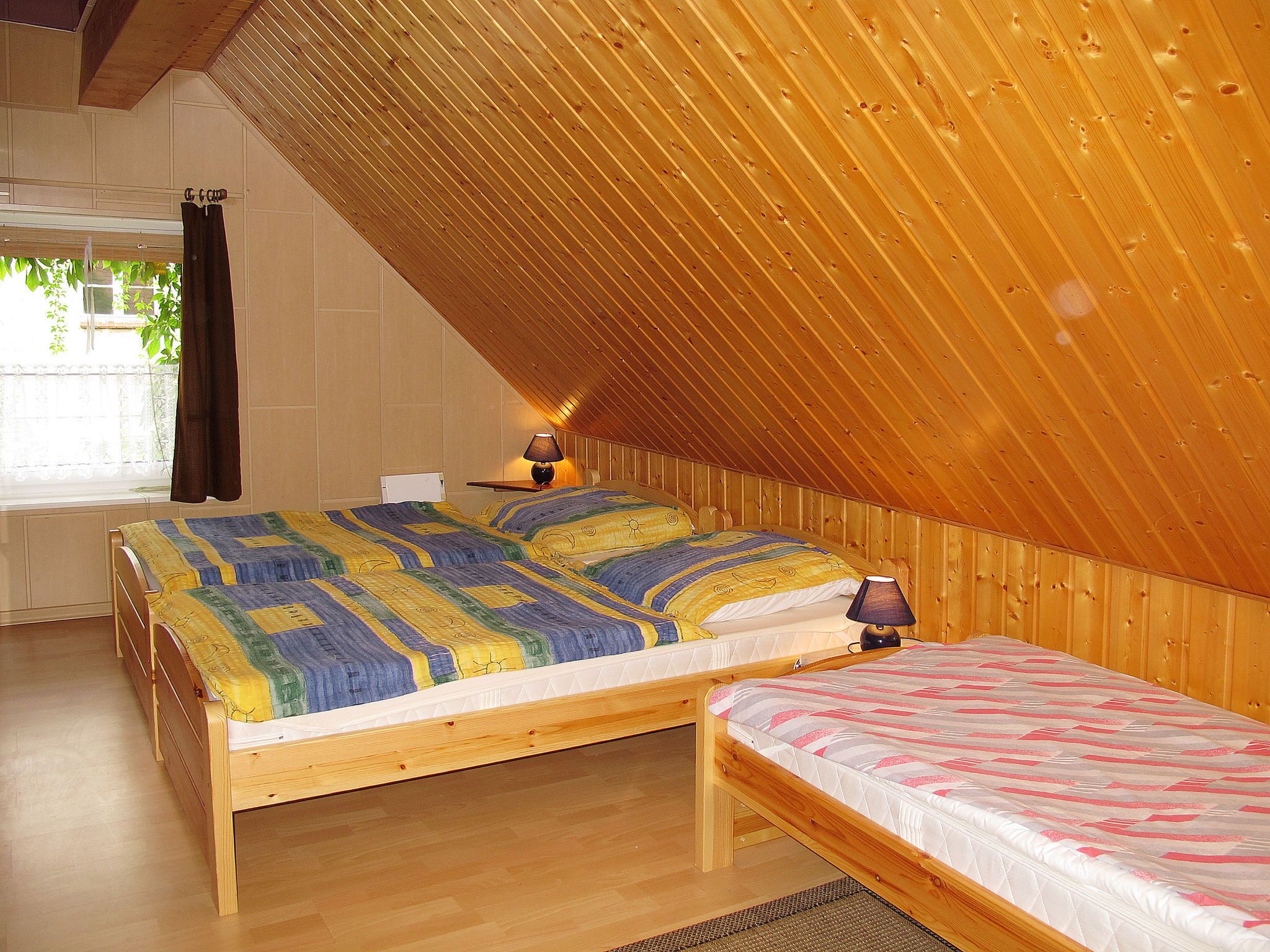Ein Schlafzimmer mit zwei Holzbetten, einem Fenster mit Vorhängen und einer schrägen Decke.