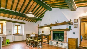 A spacious kitchen with a large dining table, wooden beams on the ceiling, and a fireplace.