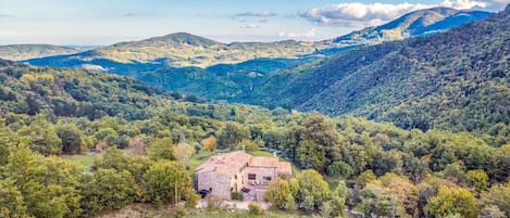 A stone house with a tiled roof surrounded by dense forest and hills.
