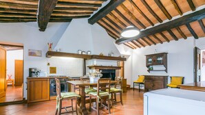 A rustic kitchen with wooden beams, a tiled floor, and a dining area with wooden chairs.