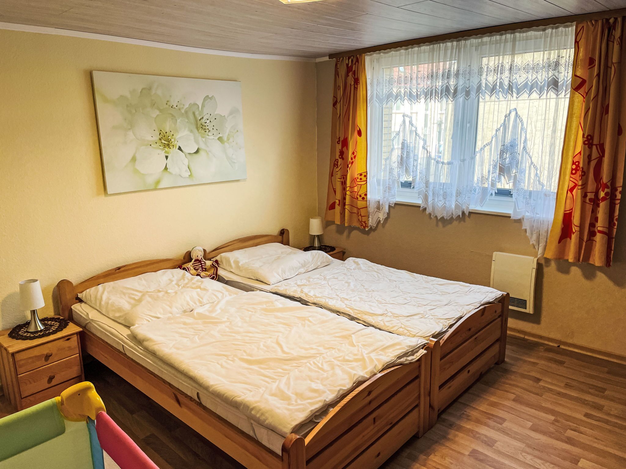 Ein Doppelbett mit Holzrahmen, ein Nachttisch mit Lampe und ein Wandbild mit Blumenmotiven.