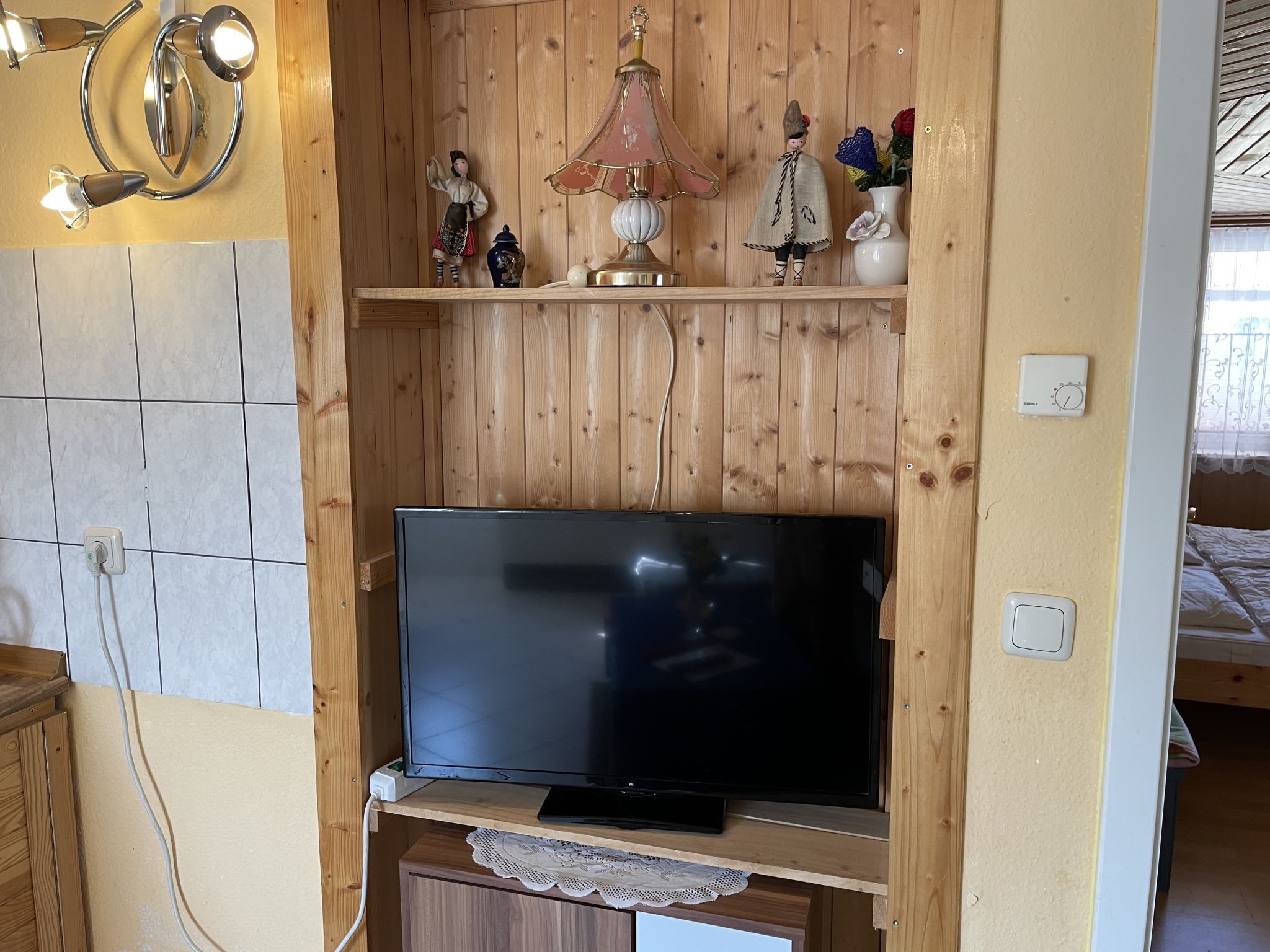 A wooden-paneled room with a television on a cabinet, a lamp, and decorative items on shelves.