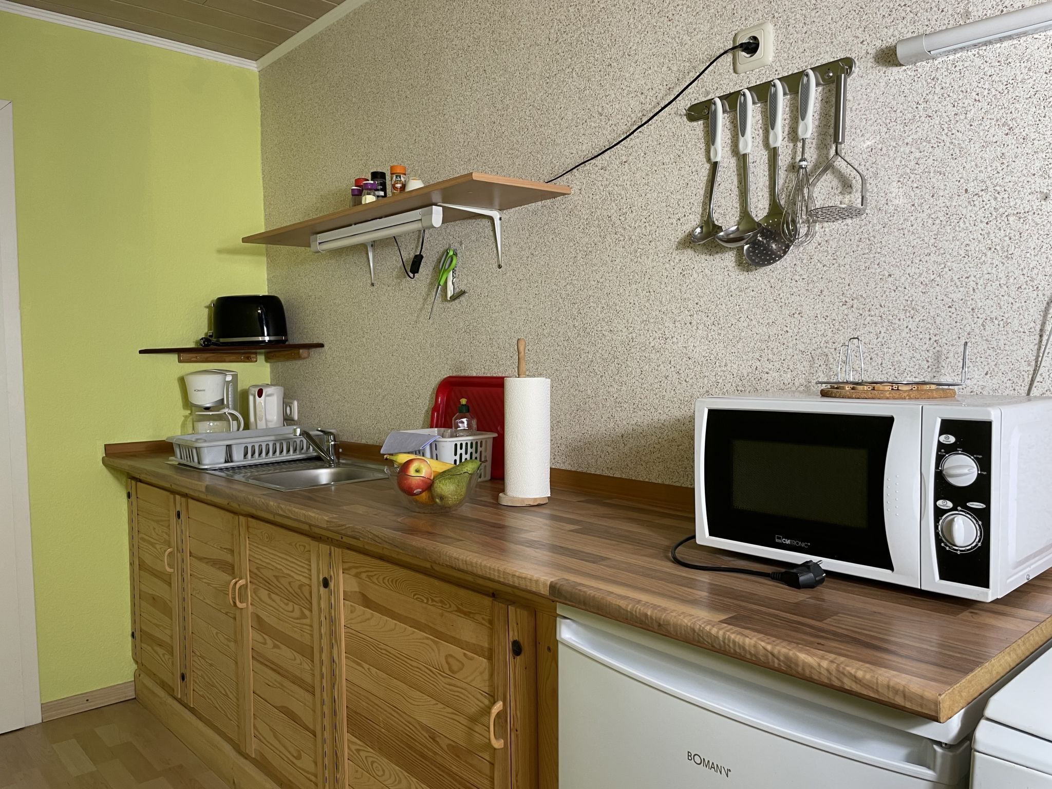 Une cuisine avec des placards en bois, un four à micro-ondes, une machine à café et divers ustensiles accrochés au mur.