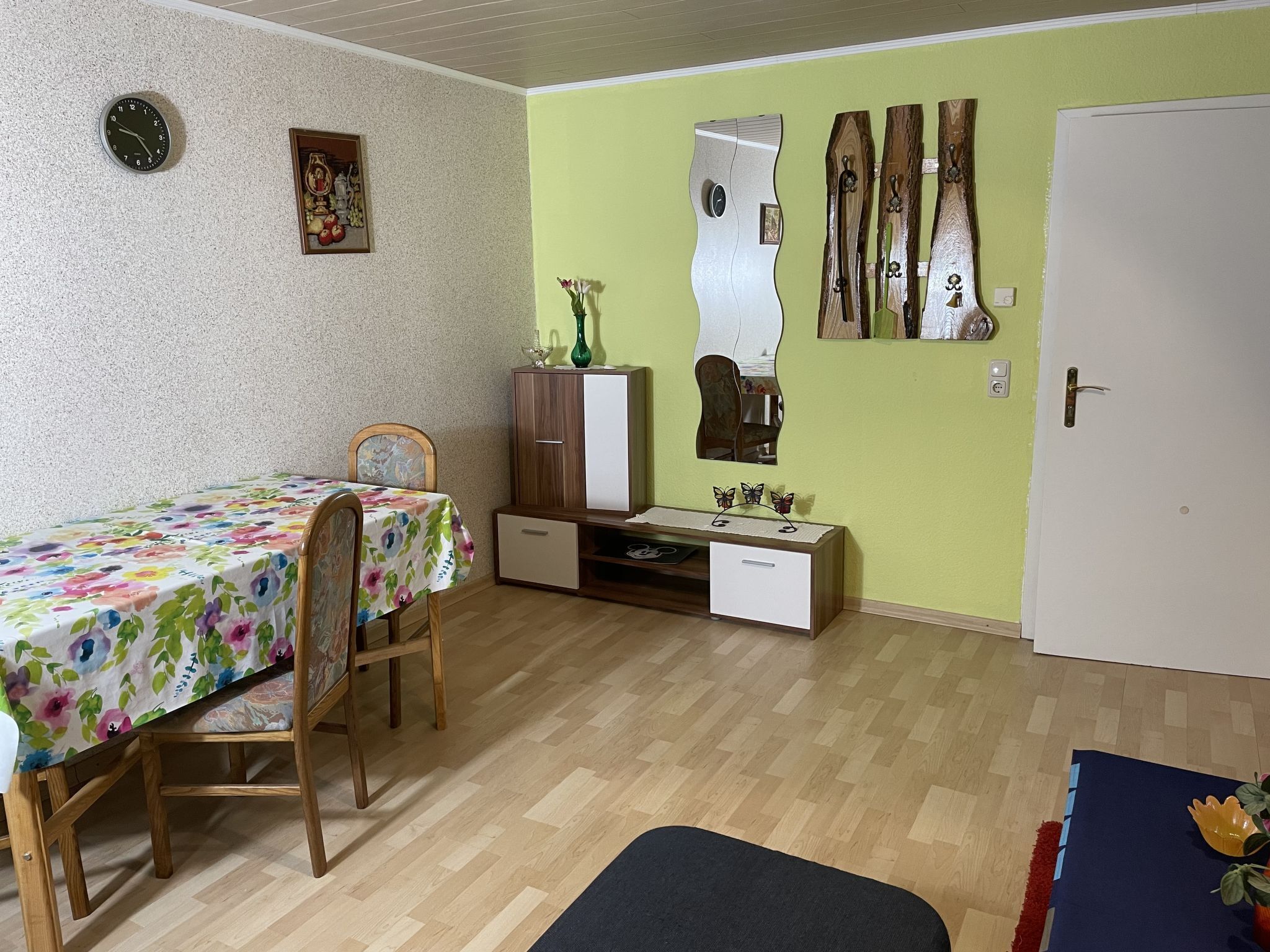 Une petite pièce bien éclairée, avec une table à manger en bois, une seule chaise, un buffet, un miroir et une porte.