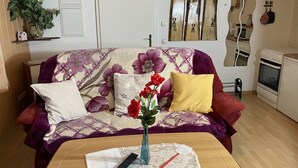 Una sala de estar con sofá, una mesa de centro, un jarrón con flores, un control remoto y un espejo montado en la pared.