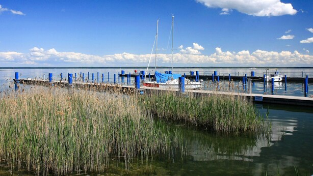Un puerto deportivo con barcos amarrados, un muelle que se adentra en el agua y un cielo despejado.