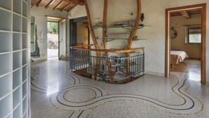 Ruime kamer met hoge plafonds, houten balken, een wenteltrap en een bibliotheek met boekenkasten.